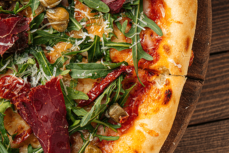 Closeup of a pizza with arugula and meat.